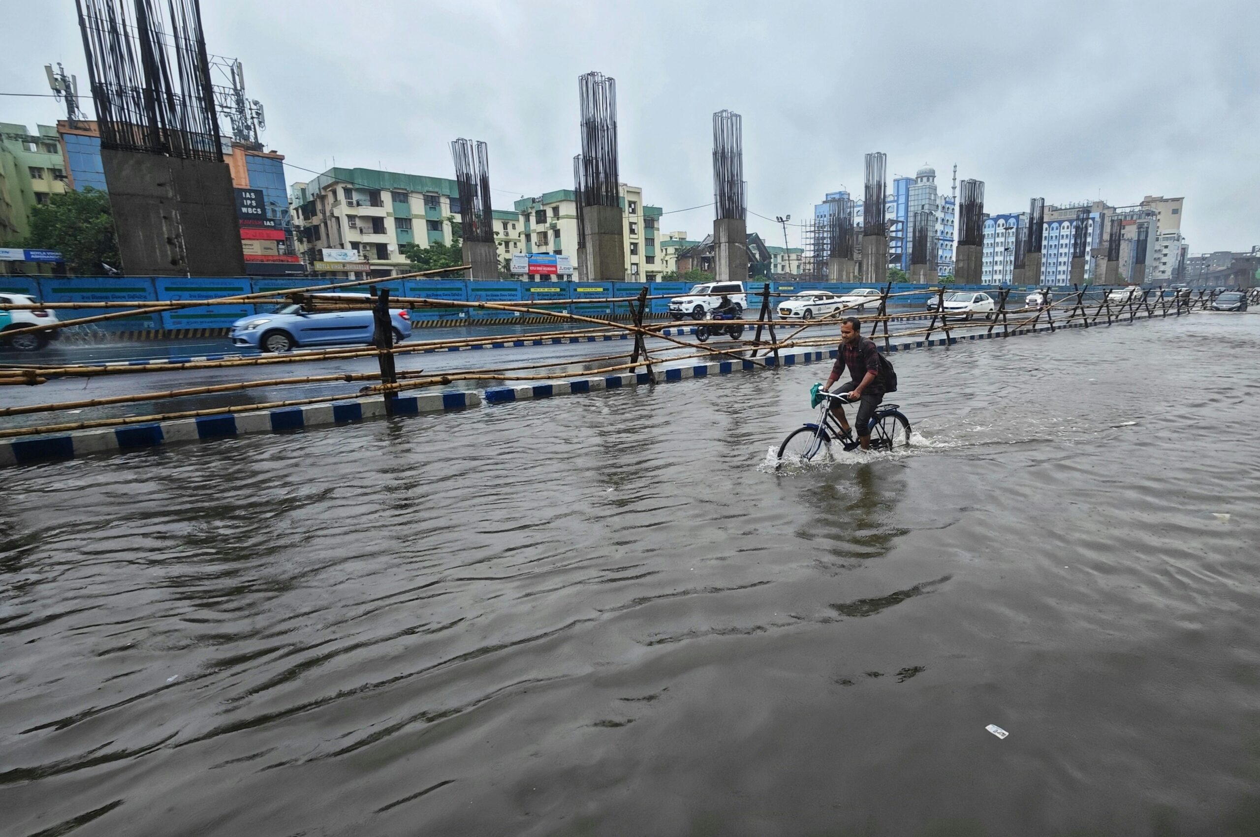 A man rides a bicycle through a flooded street in Kolkata, India, showcasing urban resilience.